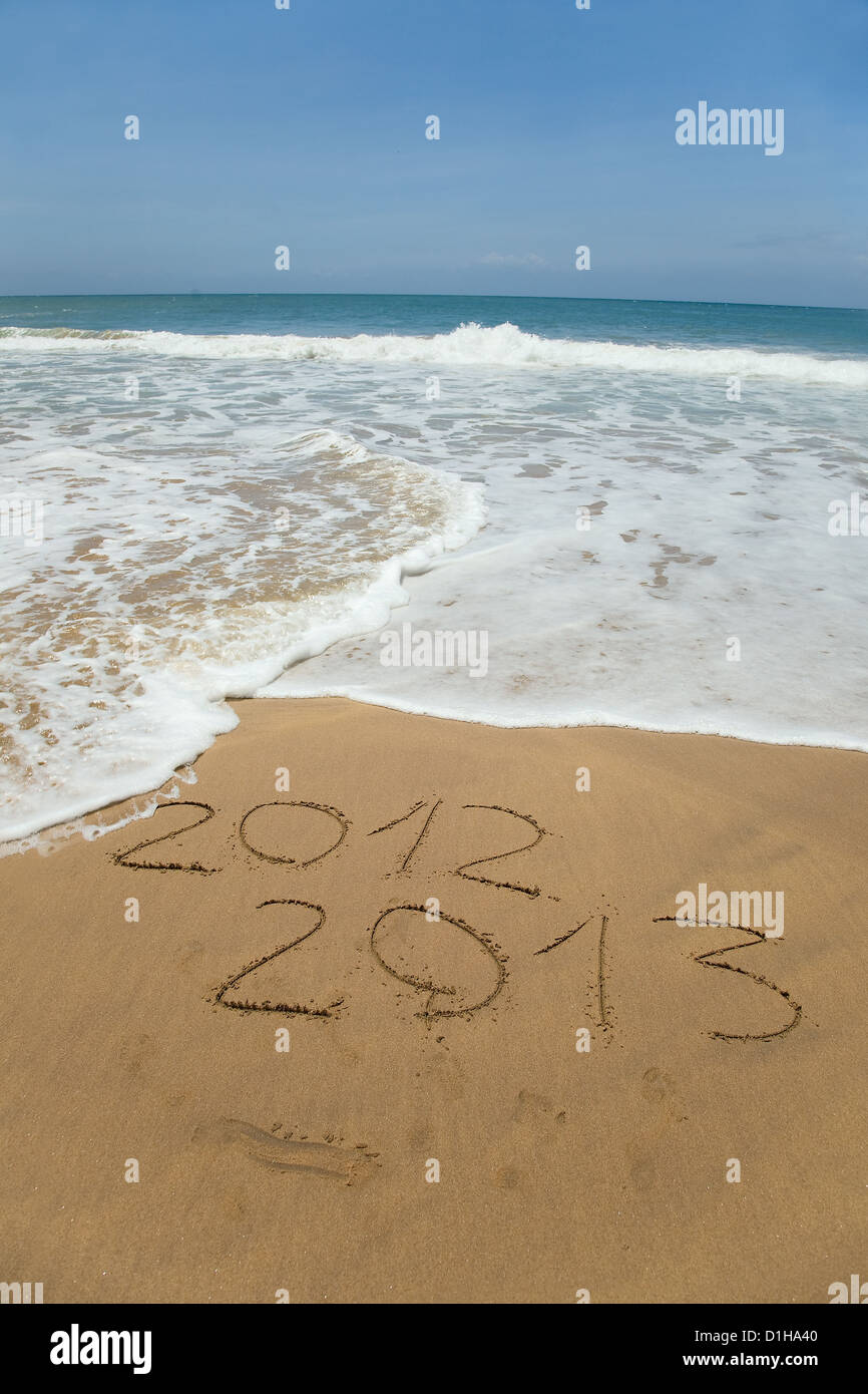 2012 and 2013 written in sand on beach with sea waves starting to erase the word Stock Photo