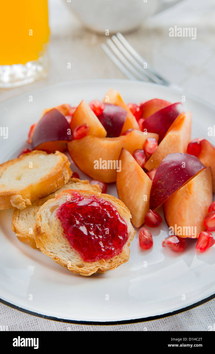 Breakfast toasts with jam, plum and pomegranate seeds, orange juice and a cup in the background Stock Photo