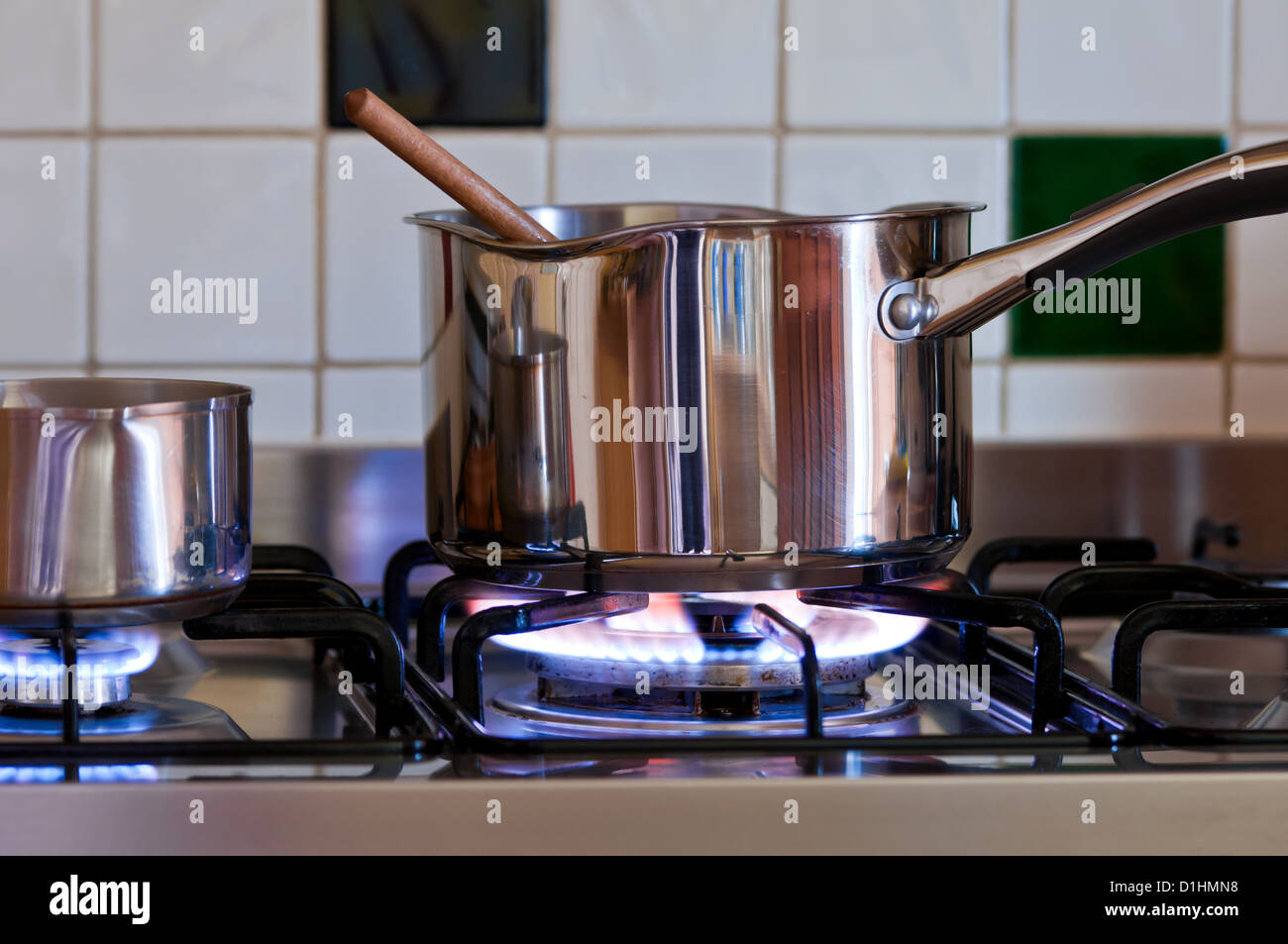 saucepans with wooden spoon on lit gas hob whilst being used for