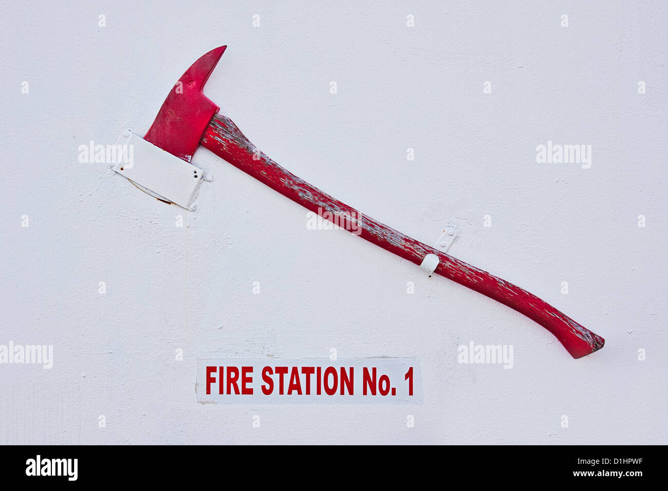 A red ax hanging on a white wall of a fire station. There is also a Fire Station sign in red letters. Stock Photo