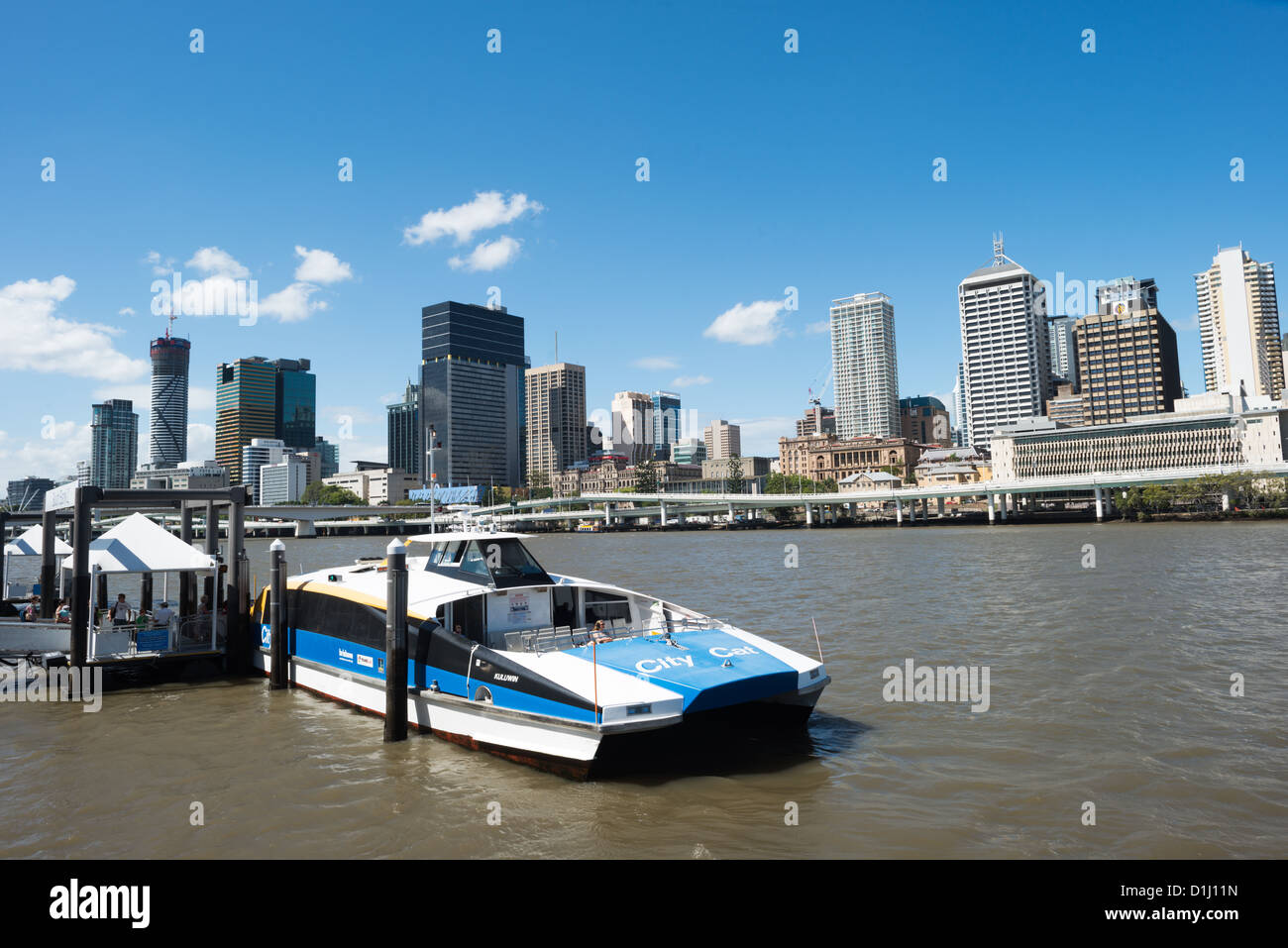 BRISBANE, Australia — A CityCat ferry approaches a terminal at South Bank on the Brisbane River, with the city's skyline visible in the background. CityCats are high-speed catamaran ferries that serve as a popular public transport option in Brisbane, connecting various riverside precincts throughout Queensland's capital city. The South Bank terminal provides access to the cultural and recreational precinct that was developed on the site of World Expo 88. The Brisbane River winds through the center of the city, with CityCat services operating along a 21-kilometer route. Stock Photo
