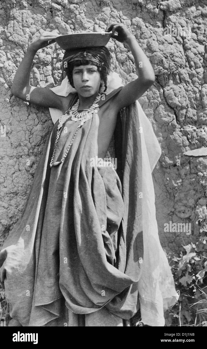 Young girl, full-length portrait, standing, facing front, wearing coin necklace, holding bowl on head, Algeria, circa 1880 Stock Photo