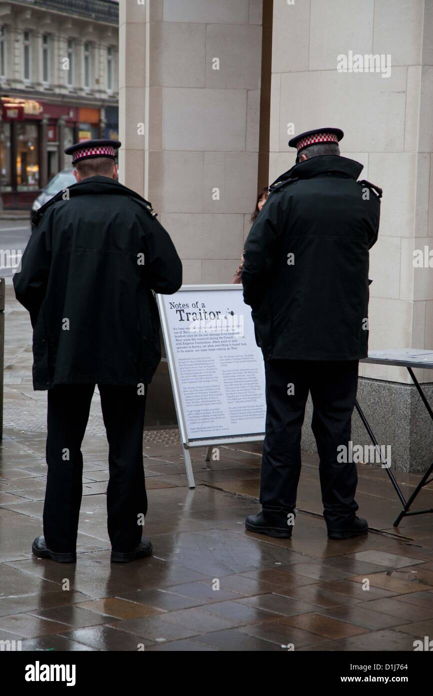 London, UK. 24th December 2012 Police officers read a board put up by a radical Muslim group outside St Paul's Cathedral. The board was put up by a group of Muslims who gathered outside the cathedral where they set up stalls and handed out leaflets with the intent to inform passers by of Islam.  There were various complaints to officers from the people queuing nearby to enter St Paul’s Cathedral where they were attending a service. Stock Photo