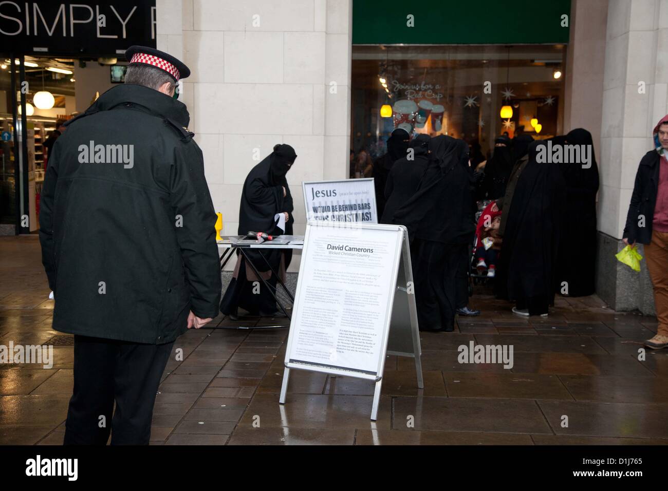 London, UK. 24th December 2012 A police officer reads a board put up by a radical Muslim group. The board was put up by a group of Muslims who gathered outside the cathedral where they set up stalls and handed out leaflets with the intent to inform passers by of Islam.  There were various complaints to officers from the people queuing nearby to enter St Paul’s Cathedral where they were attending a service. Stock Photo