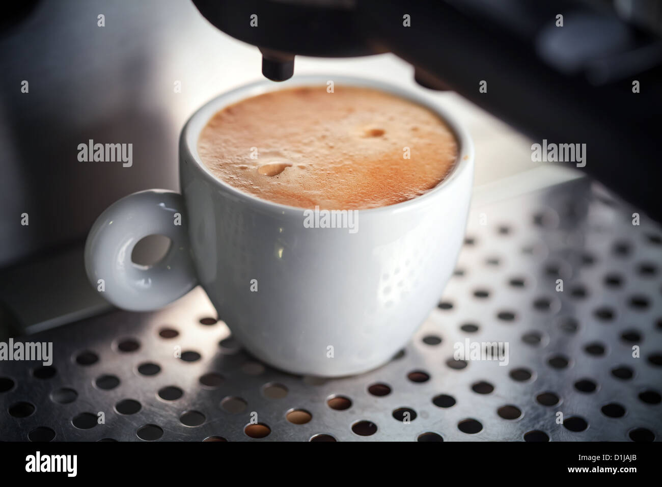 White ceramic cup of fresh espresso with foam in the coffee machine. Stock Photo