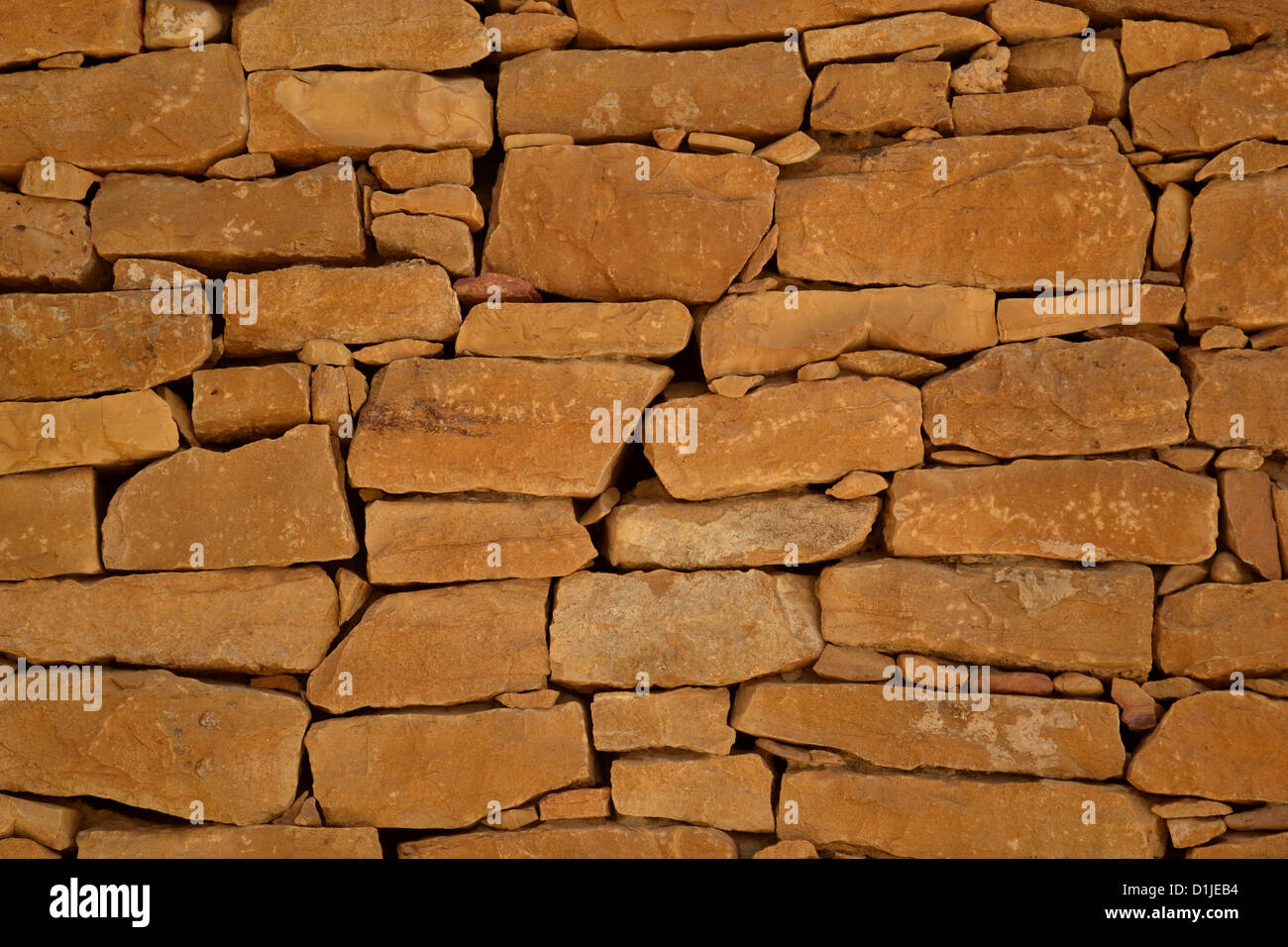 A stone wall built by wedging small stones in between the gaps of bigger sandstones. Stock Photo