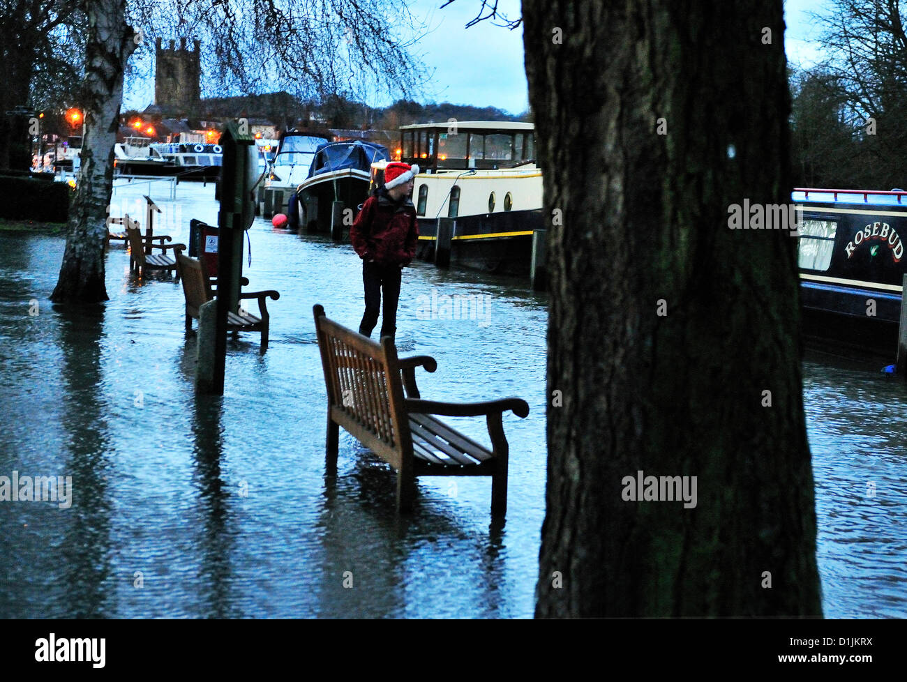 Henley-on-Thames Buckinghamshire   UK   17.00 GMT  20-12-2012   A Santa reveler  not  thwarted by the rising flood waters  and takes a traditional Christmas Day walk (wade0 along the Thames side tow path at Mill Meadows ,Henley-on-Thames,   seen with Saint Mary's Church  Henley-on-Thames behind Stock Photo