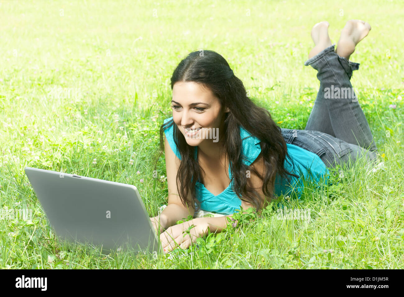 Portrait of a cute young female lying on the grass in the park using a ...