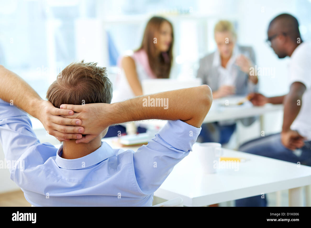 Rear view of relaxed teacher keeping hands behind head and looking at ...