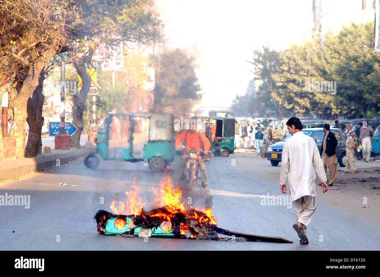 KARACHI, PAKISTAN, DEC 26: Commuters pass through near fire lighten by angry protesters  during strike called by Ahle Sunnat Wal Jamat (Defunct Sipah-e-Sahaba) against an  assassination attack on their leader Aurangzeb Farooqi convoy and killing of his seven gunmen  and driver, at Patel Para area in Karachi on Wednesday, December 26, 2012.  (S.Imran Ali/PPI Images). Stock Photo
