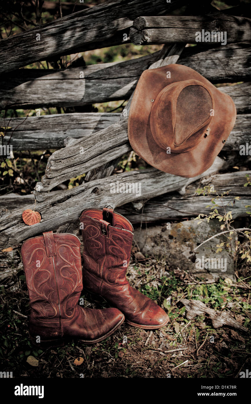 Cowboy hat and cowboy boots with old log fence. Stock Photo