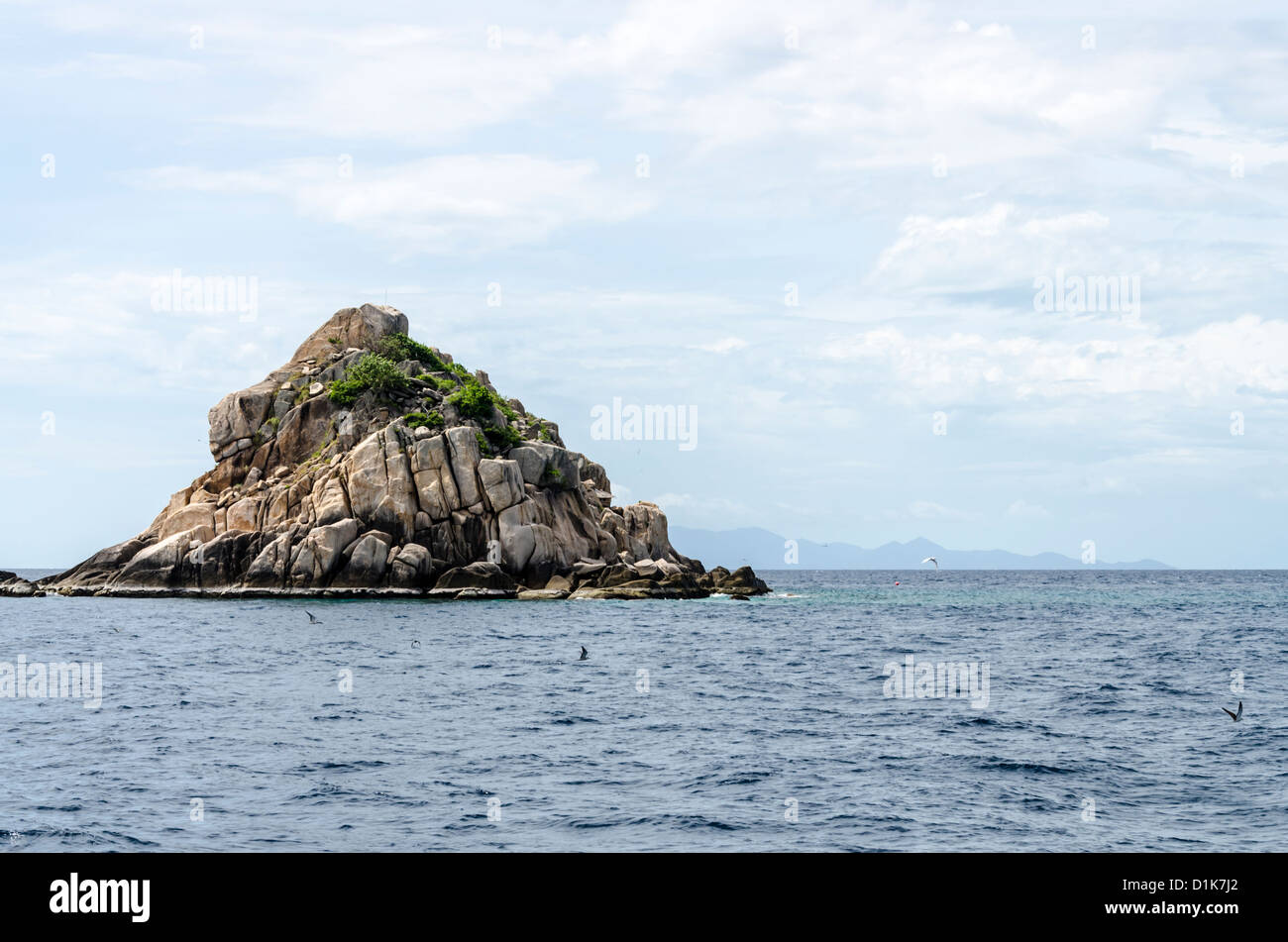 Small rocky island with large boulders up close in sunshine and Koh Pha-Ngan in distance in the Gulf of Thailand near Koh Tao Stock Photo