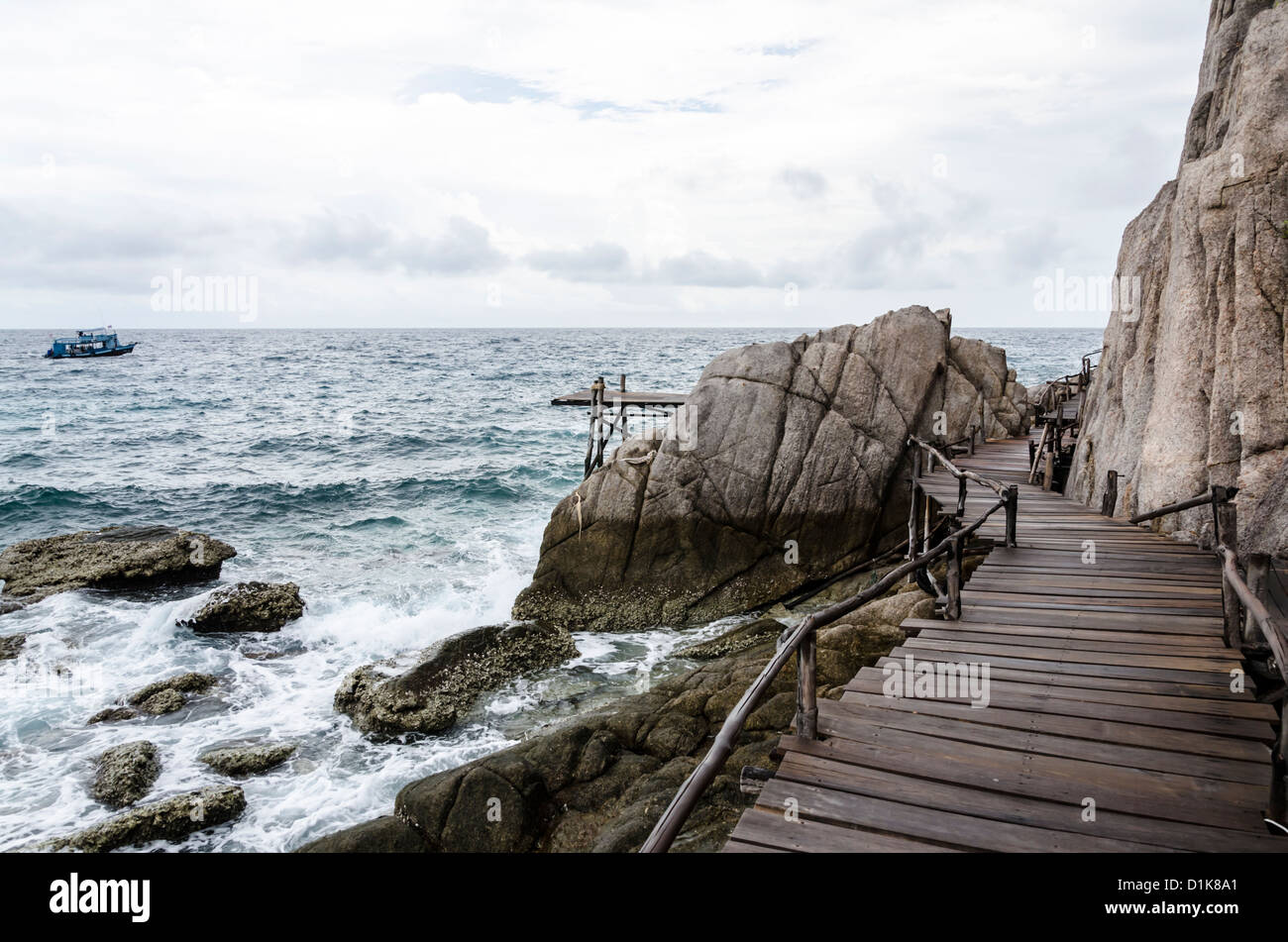 Rickety boardwalk and wooden pier and stormy sea with boat in background on Ko Nang Yuan in the Gulf of Thailand Stock Photo