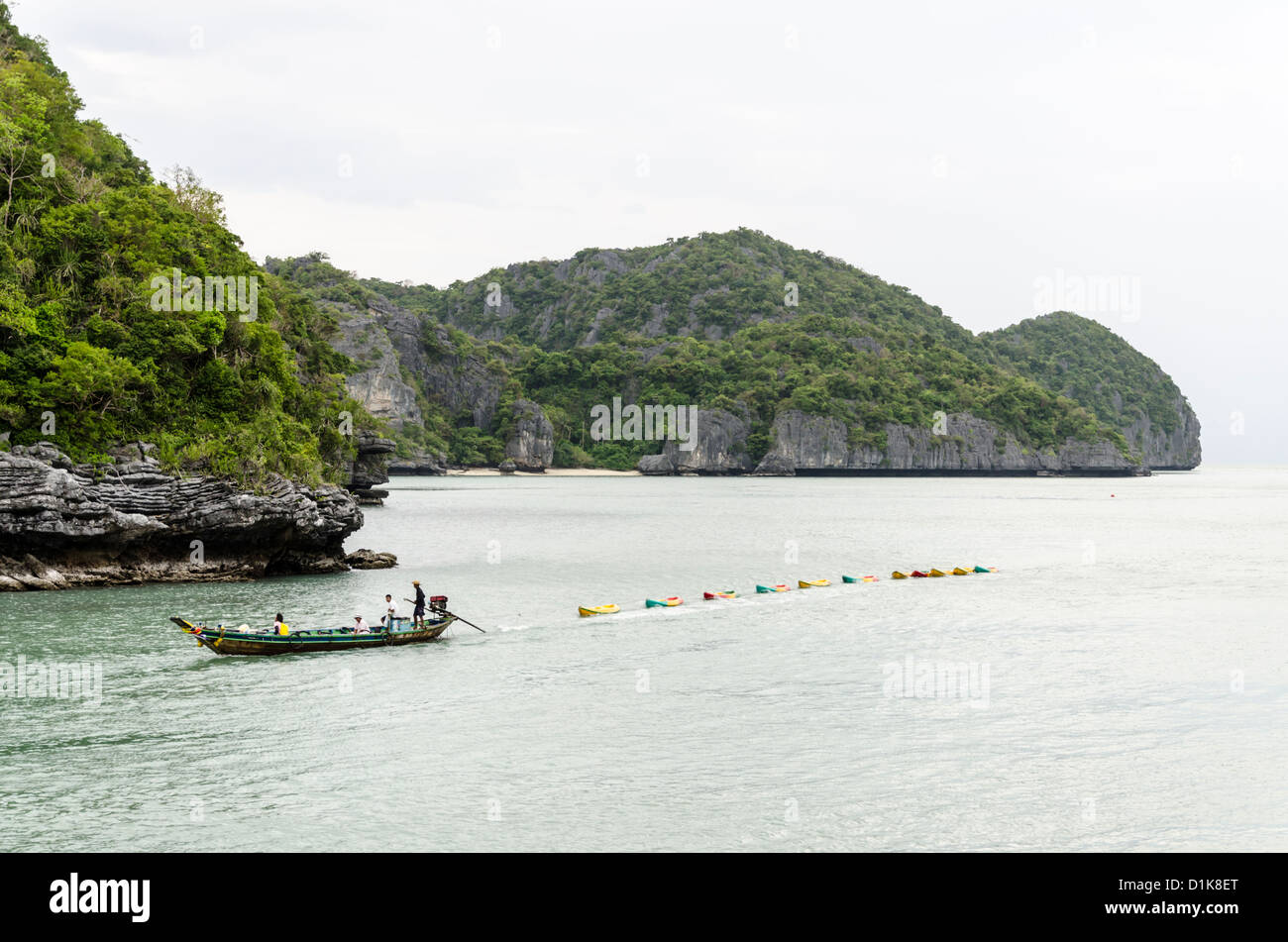 Longtail boat pulls 11 sea kayaks by islands with limestone cliffs in Ang Thong Marine National Park in southern Thailand Stock Photo