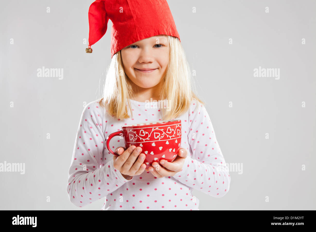 Studio portrait of happy young girl wearing red Christmas elf hat and holding a big red cup Stock Photo