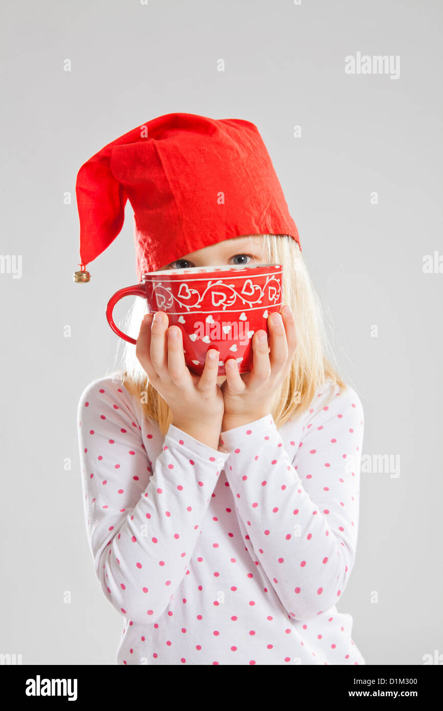 Studio portrait of happy young girl wearing red Christmas elf hat and holding a big red cup Stock Photo