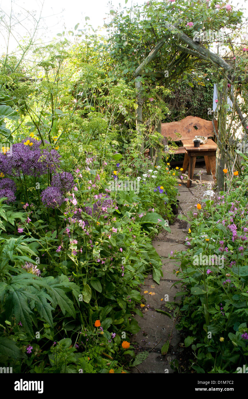 Paved path leading through herbaceous early summer borders to the relaxing area, Cottage Farm Stock Photo