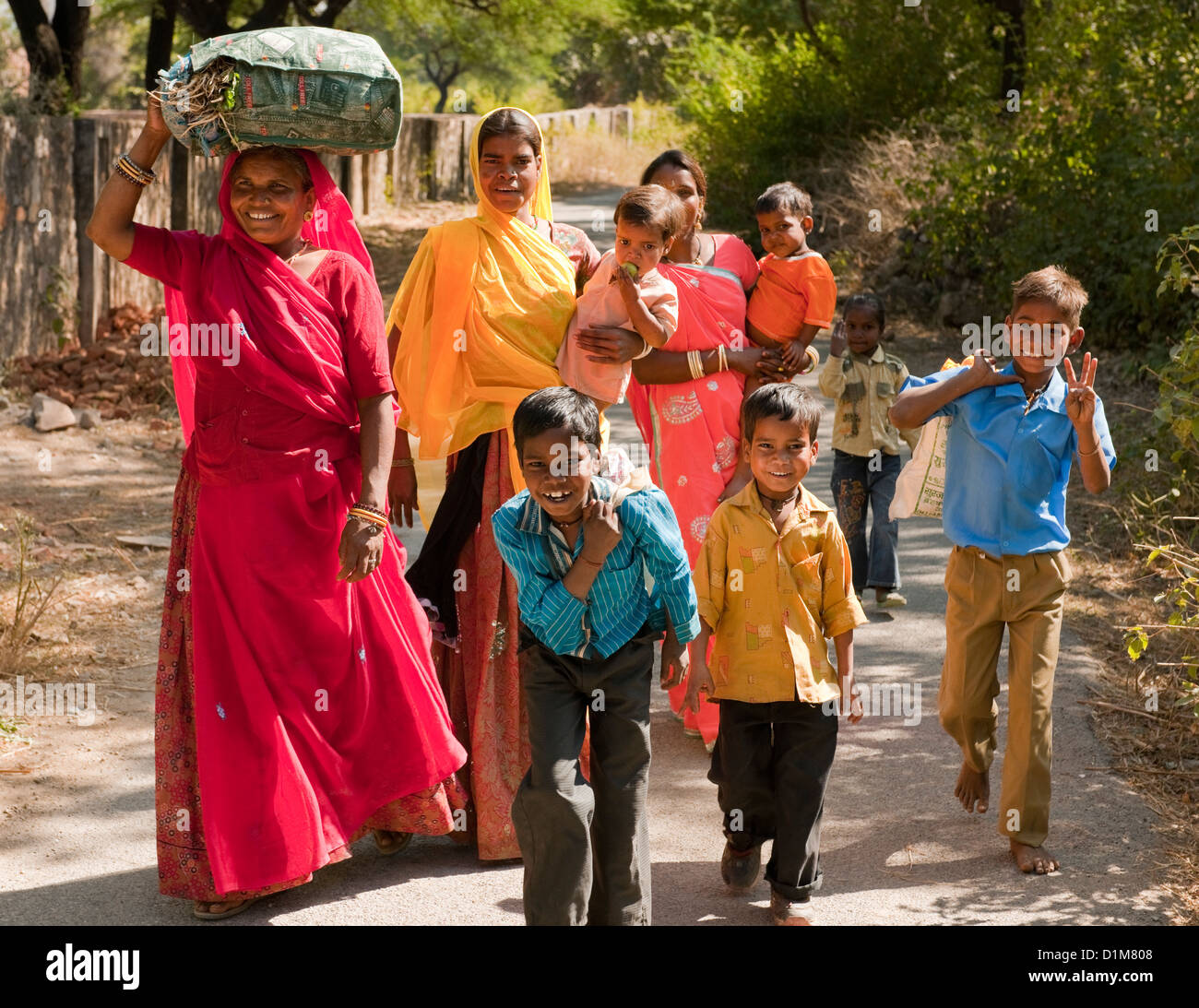 A happy smiling colorful Indian family group of women boys girls and a baby return from shopping on a quiet road in India Stock Photo