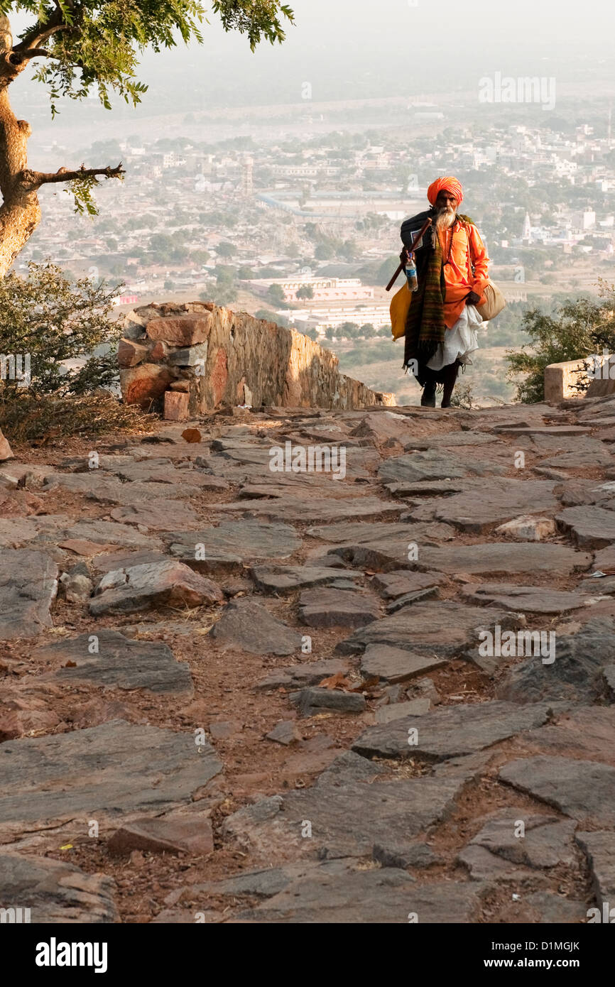 A Sadhu (Hindu holy man) walking on a cobbled path in his orange robe and turban near Pushkar Rajasthan India Stock Photo