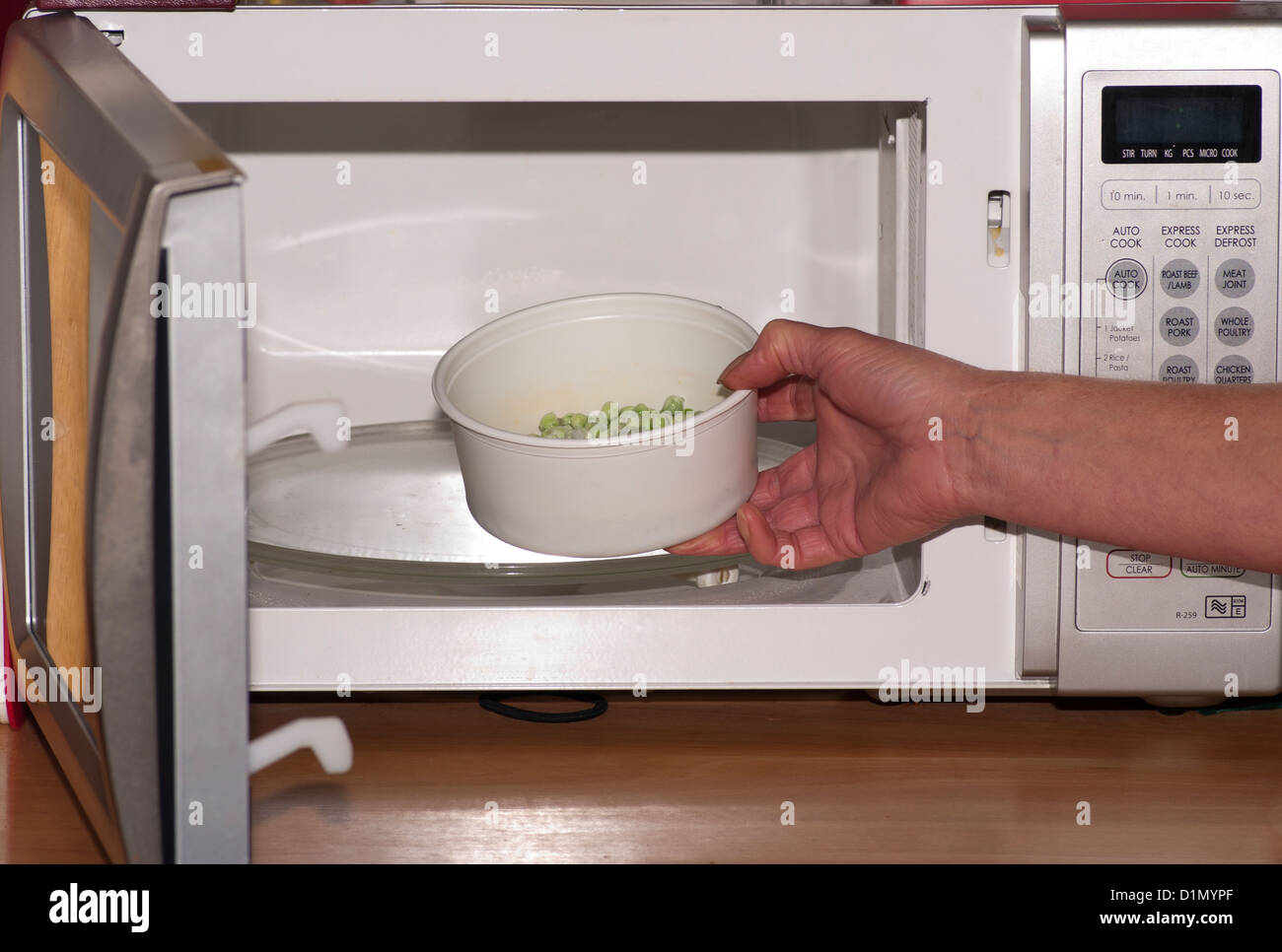 Woman Putting Peas vegetable Into A Microwave Oven Stock Photo