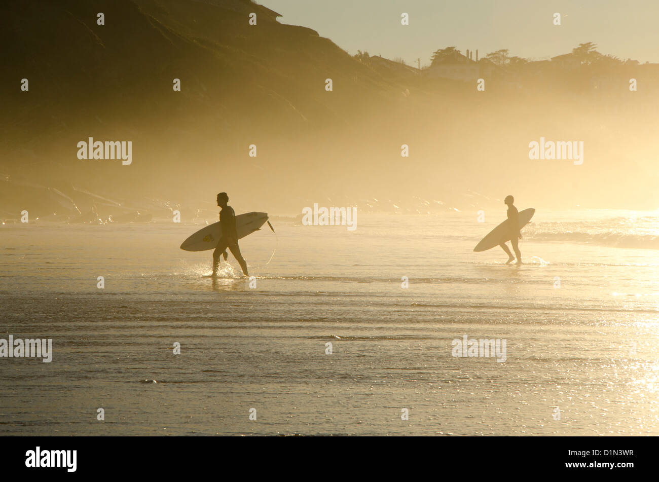 Surfers leaving the waves behind at a beach near Biarritz during sunset, France. Stock Photo
