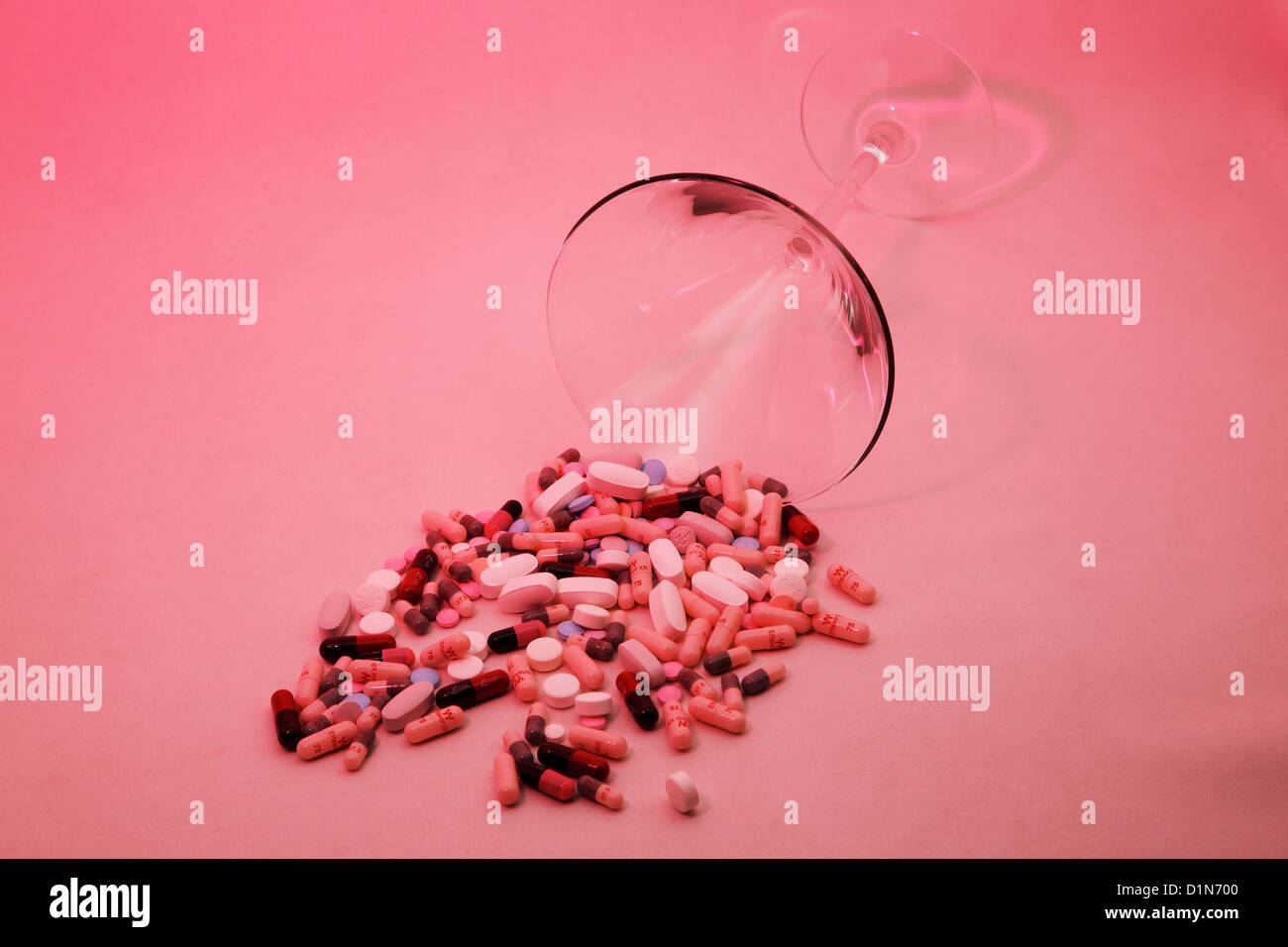 Prescription pills, tablets, capsules spilling from martini glass. Red background Stock Photo