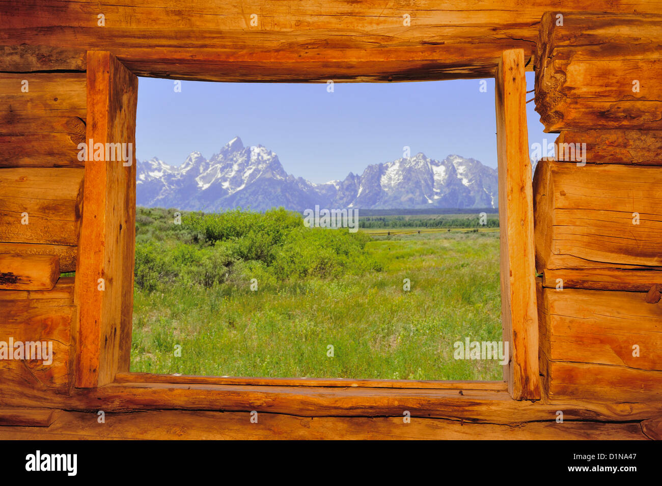 A view of the Grand Tetons mountain range from inside the window of an old log cabin. Stock Photo