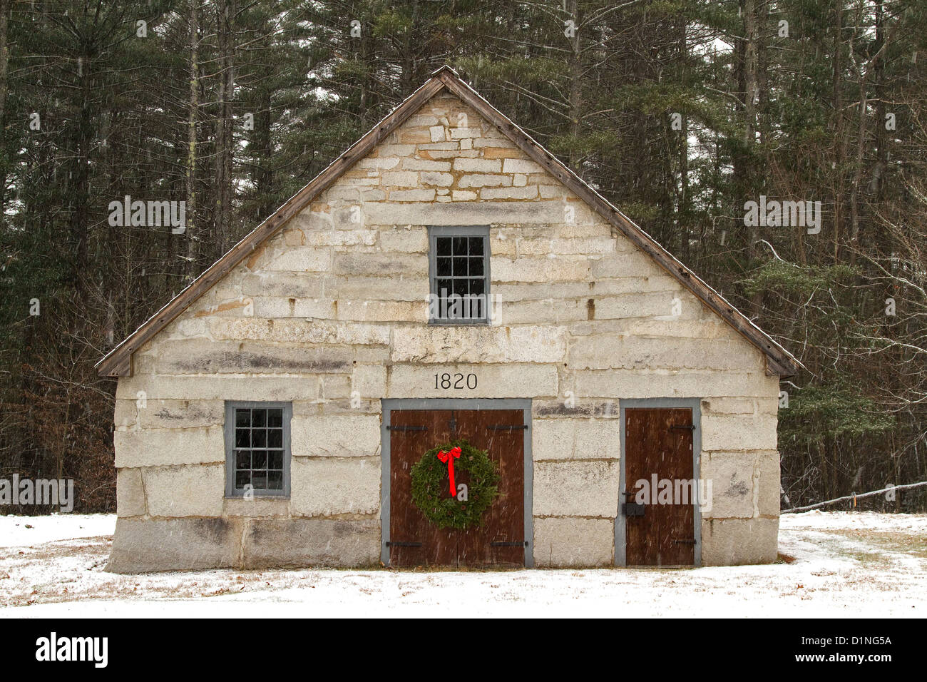 Christmas wreath decorates a wooden door of an old stone barn in a Christmas scene with falling snow in New England. Stock Photo