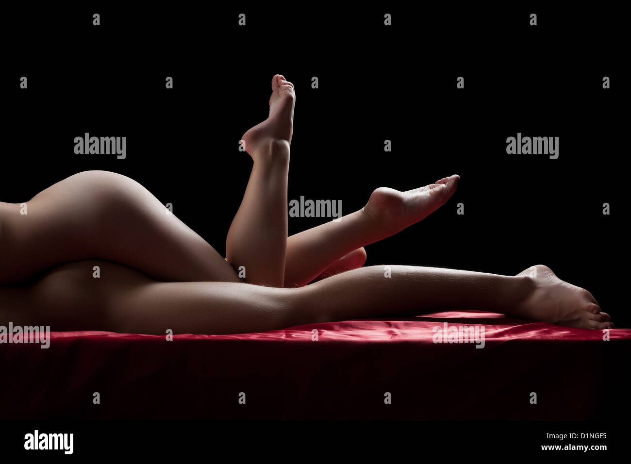 Sexy legs of couple having sex on red sheet Stock Photo
