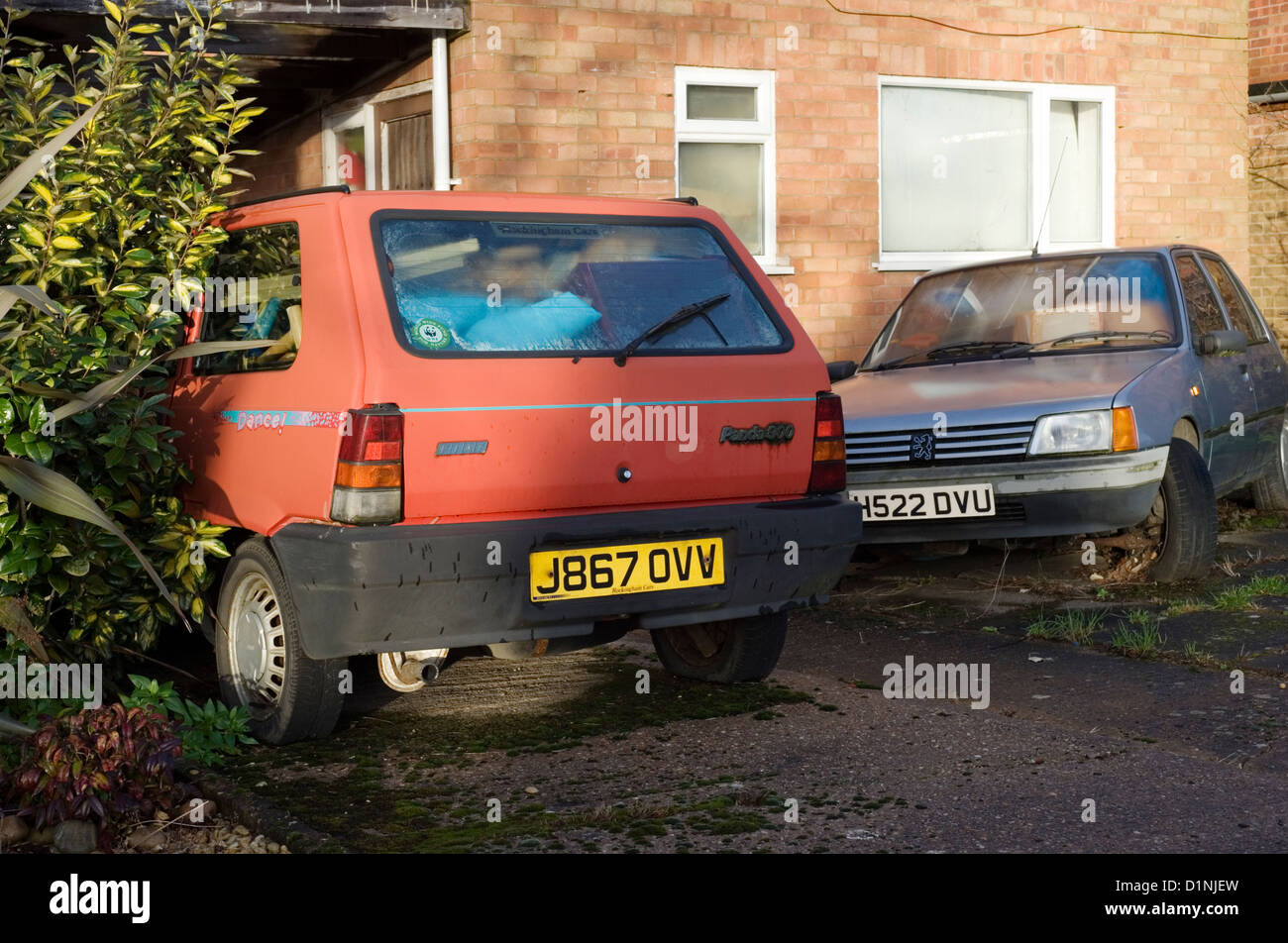 dilapidated cars used for storing junk in front of run down house Stock Photo