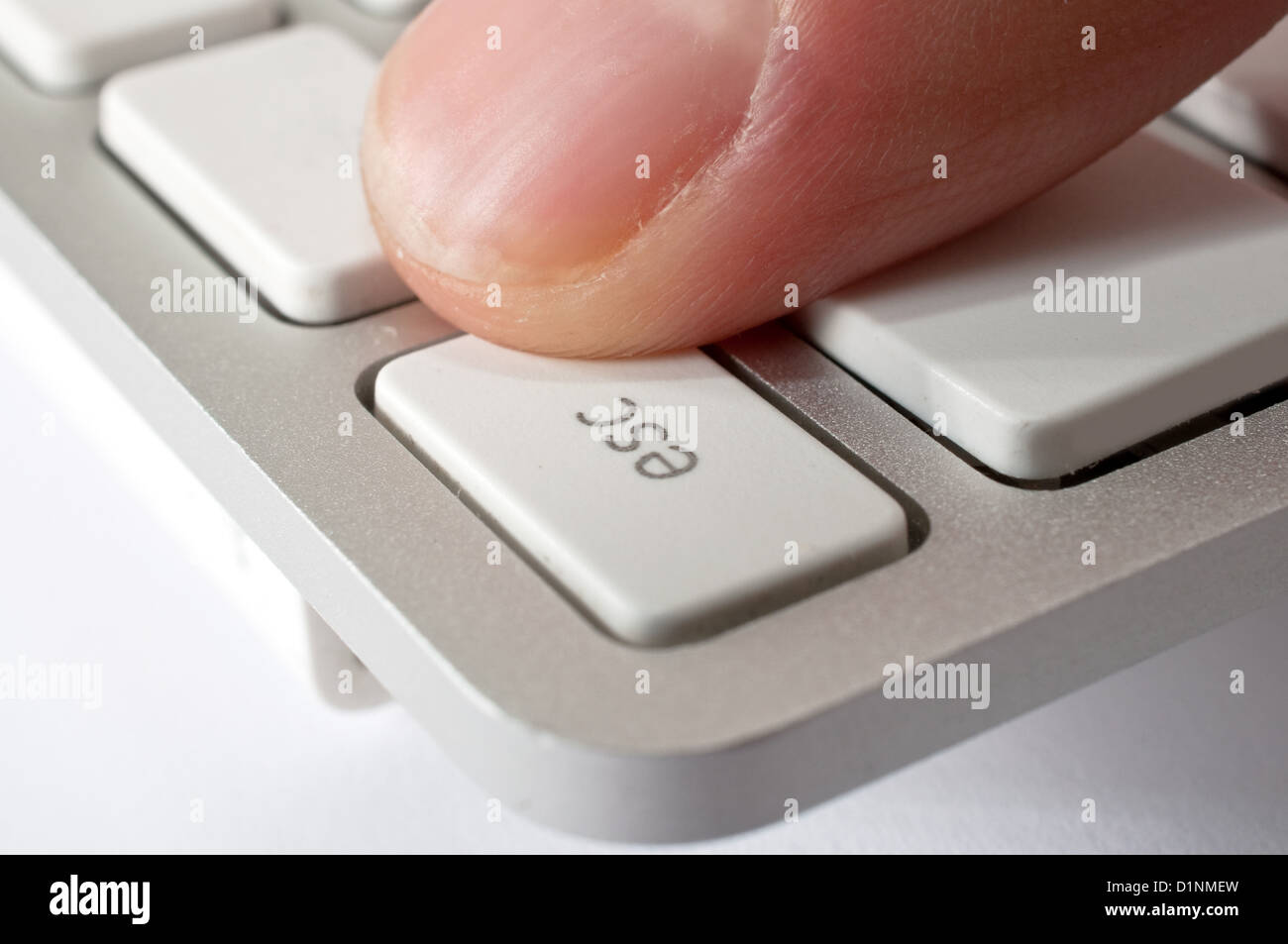 Finger is pressing ESC key of a modern stylish aluminium white computer keyboard Stock Photo