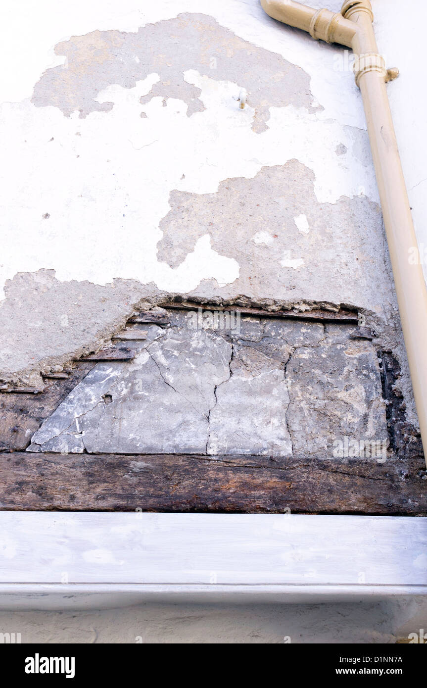 Looking up at section of concrete render that has fallen away from house wall revealing original timbers Stock Photo