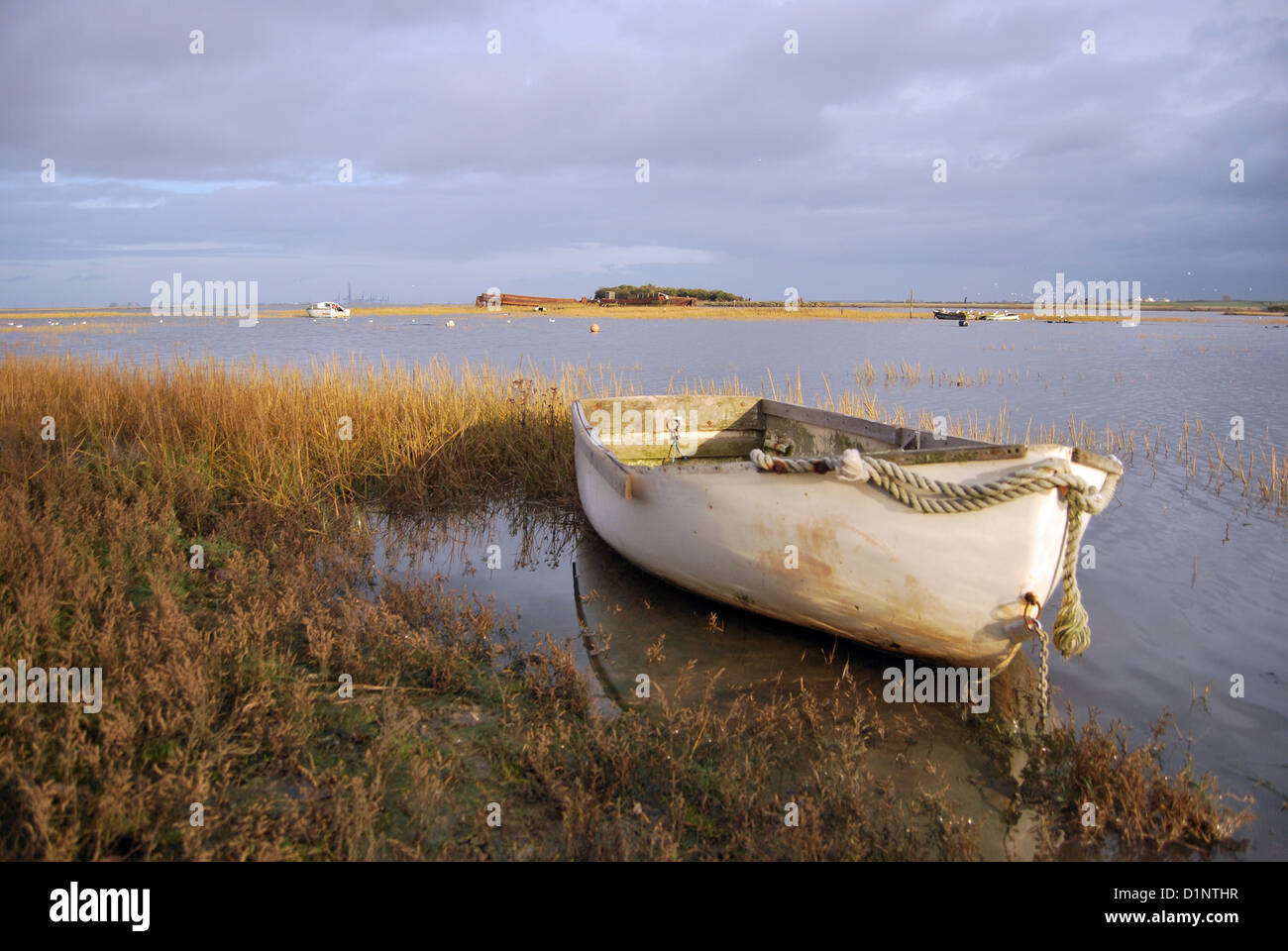 A small rowing boat floats on the rising tide with reeds around it on a cloudy day at Riverside