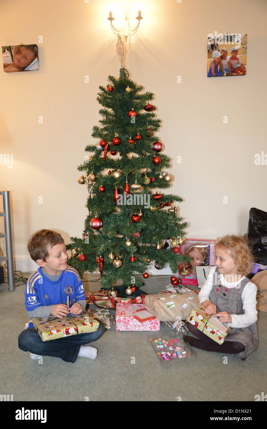 Young boy and girl opening presents by Christmas tree, Kingston upon Thames, Greater London, England, United Kingdom Stock Photo