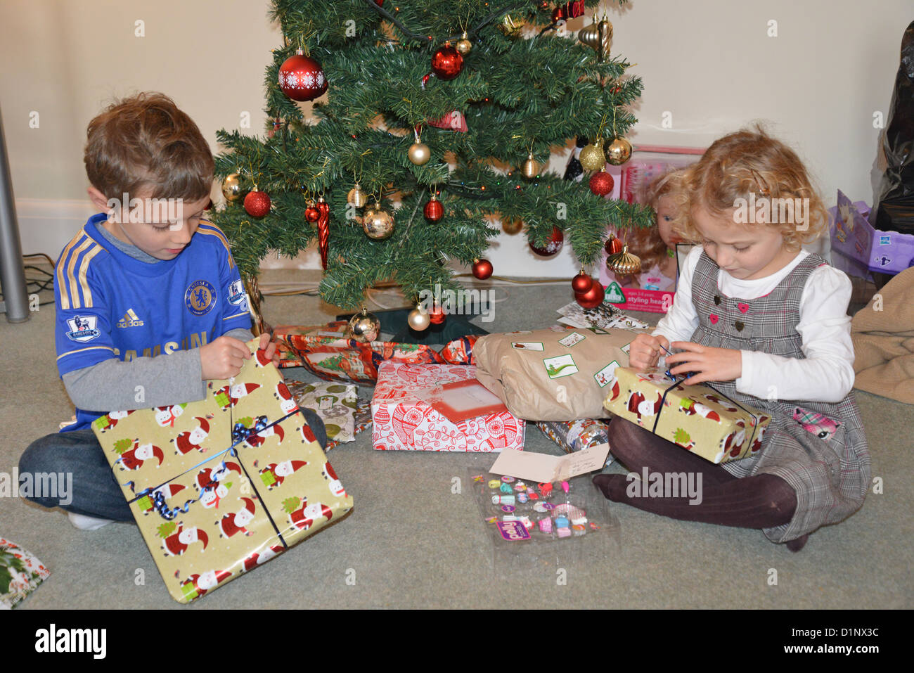 Young boy and girl opening presents by Christmas tree, Kingston upon Thames, Greater London, England, United Kingdom Stock Photo
