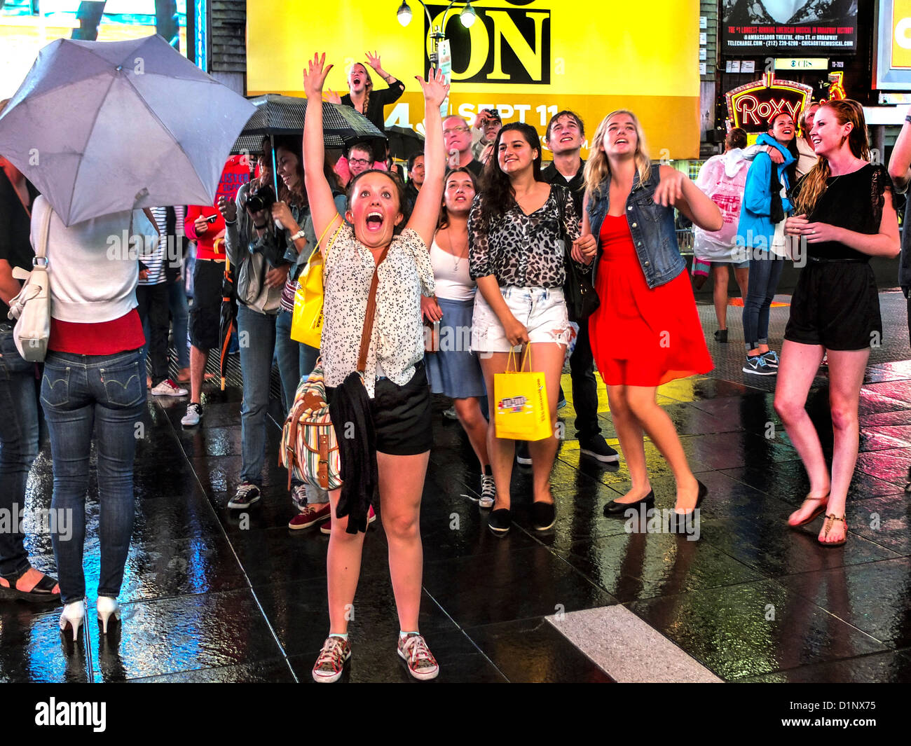 Happy teen girls watch themselves dance before a television camera projecting their image onto a huge screen in Times Square NYC Stock Photo