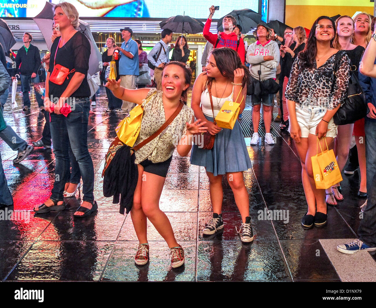 Happy teen girls watch themselves dance before a television camera projecting their image onto a huge screen in Times Square NYC Stock Photo