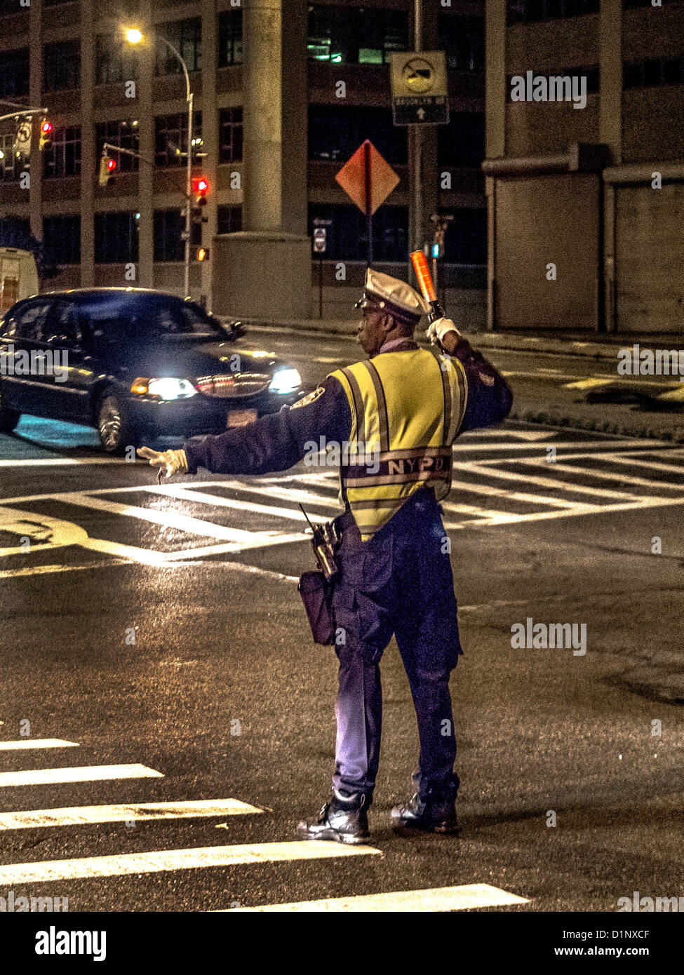 An African American policeman directs traffic at night in New York City in a safety vest. Stock Photo