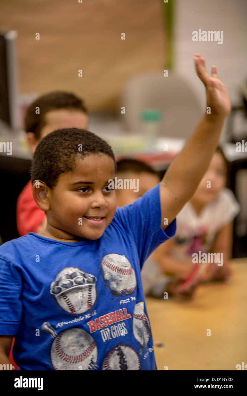 An enthusiastic hearing-impaired African American elementary school boy holds up his hand in class in Riverside, CA. Stock Photo