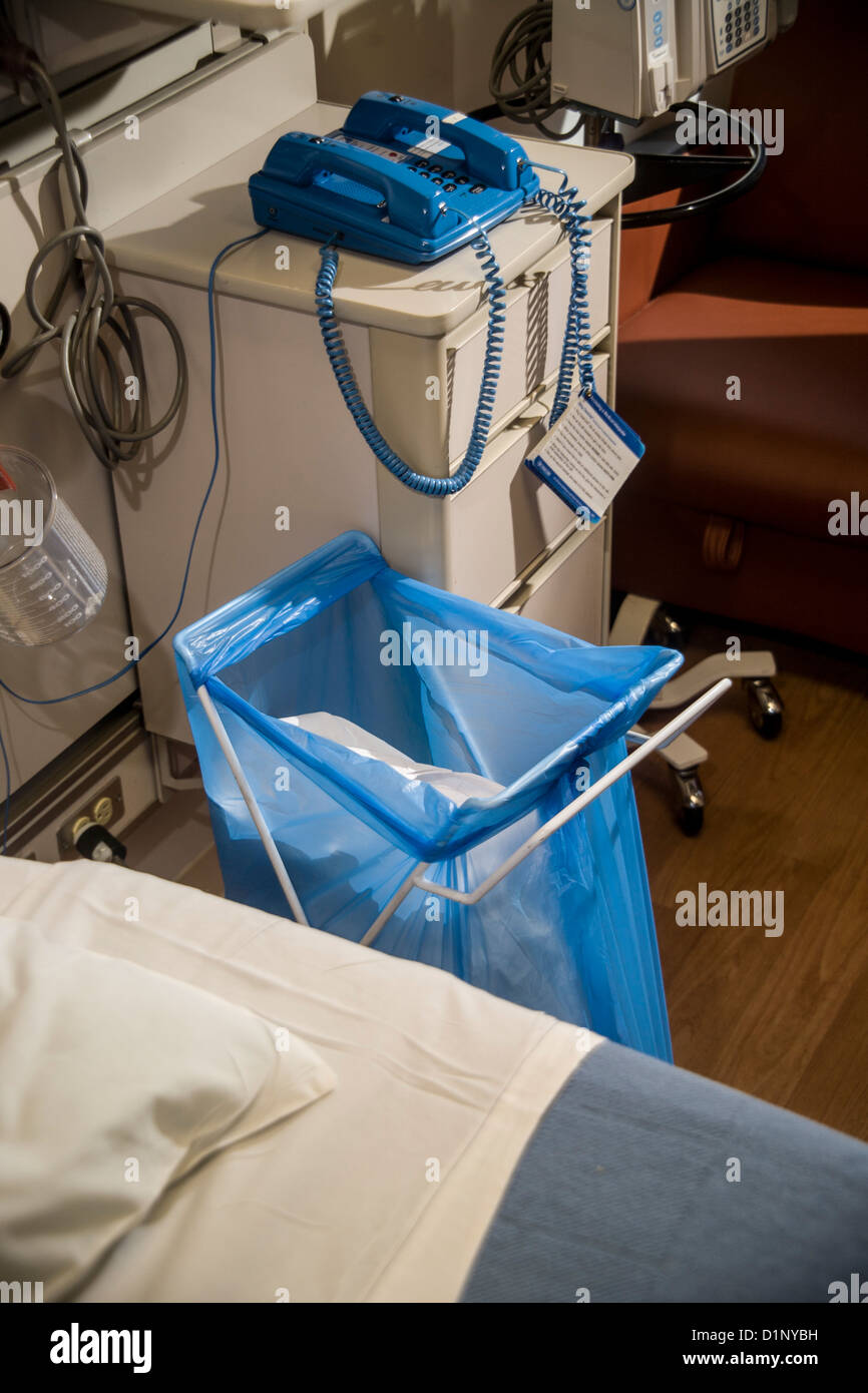 A full blue disposal bag stands beside a patient's bed in an in Orange