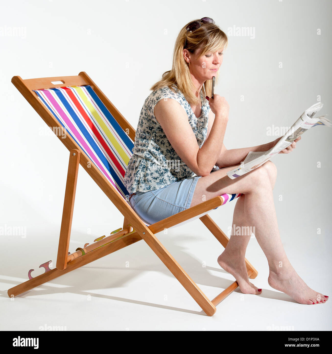 Mature woman sitting in a deckchair reading a newspaper Stock Photo - Alamy