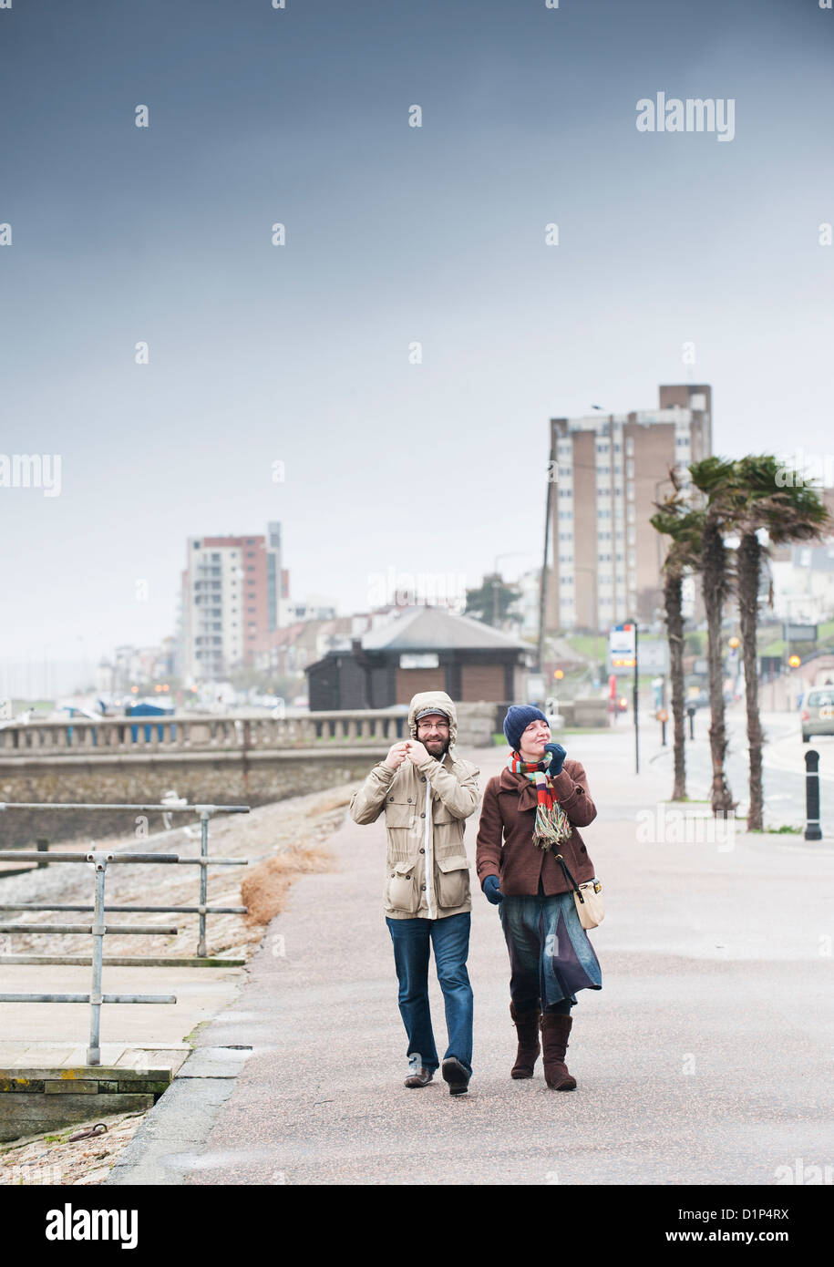 A couple walking along a seafront in windy conditions. Stock Photo