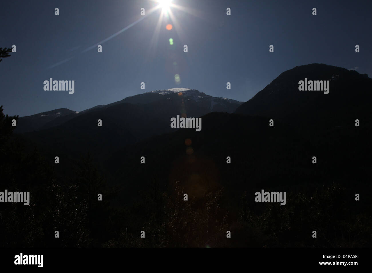 Sun shining on snow-topped mountain range in silhouette,Serra de Collserola, Spain Stock Photo