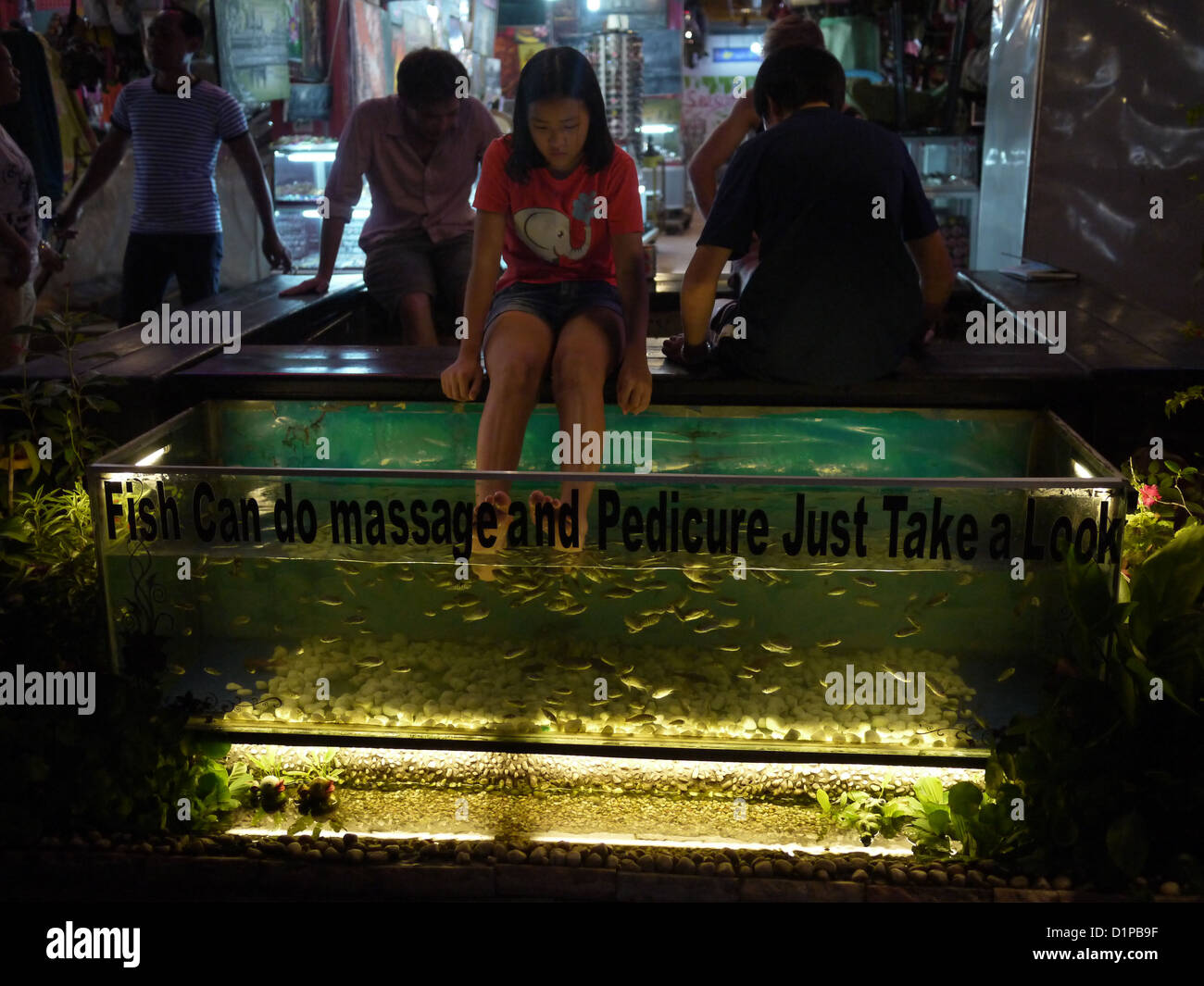 young girl dipping feet into tank with fish eating away dead or dry skin Stock Photo