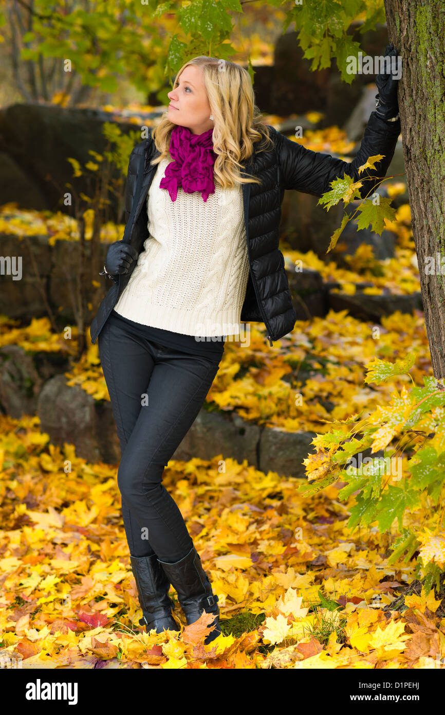Beautiful girl leans on tree, several leaves on the ground Stock Photo