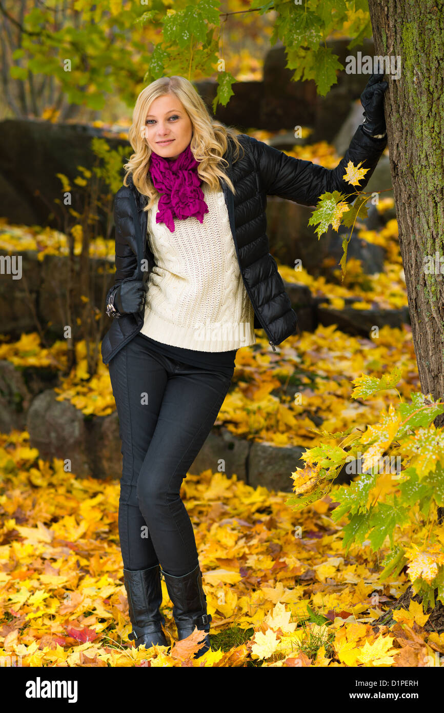Beautiful girl leans on tree, several leaves on the ground Stock Photo