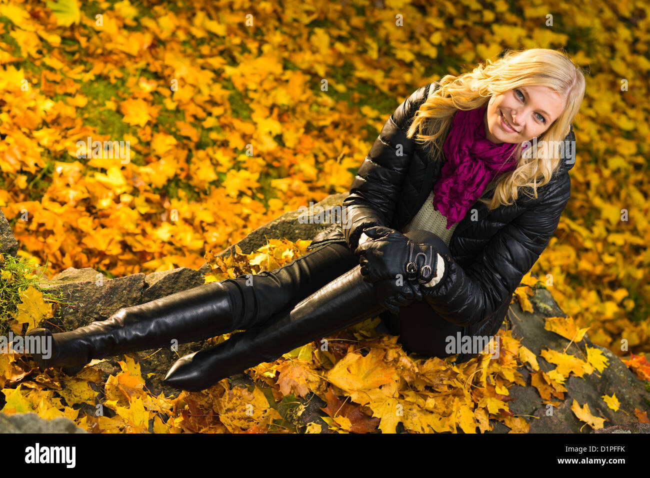 Beautiful girl sitting on a rock, autumn color leaves on the background, horizon format Stock Photo