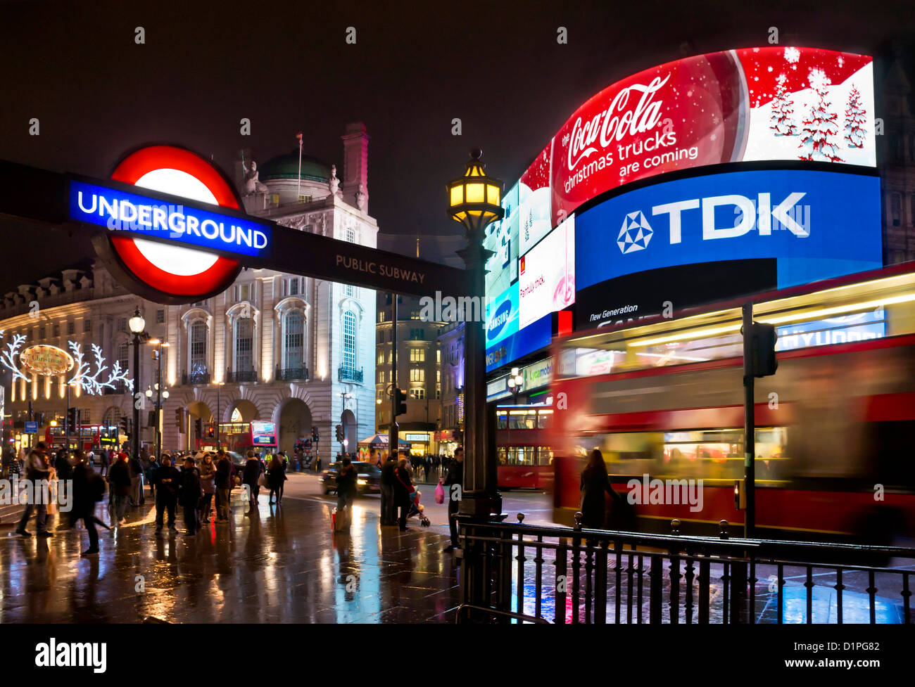 Busy People and a blurred Red London bus on a Busy night near Piccadilly Circus Underground Station Sign Central London England GB UK Europe Stock Photo