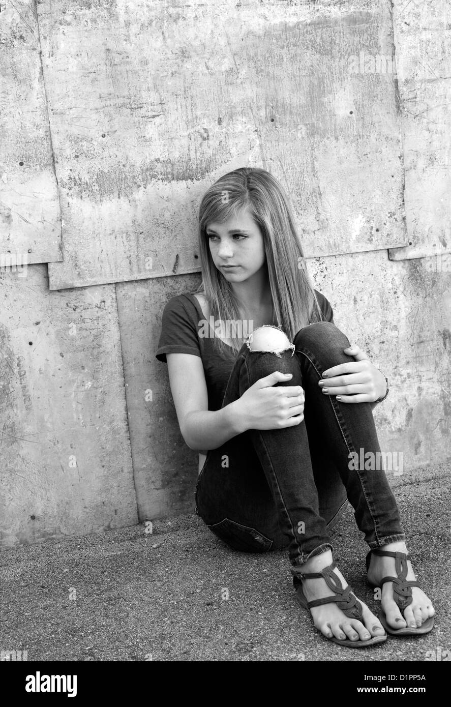 Sad teenage girl sitting on the ground in alleyway. Stock Photo
