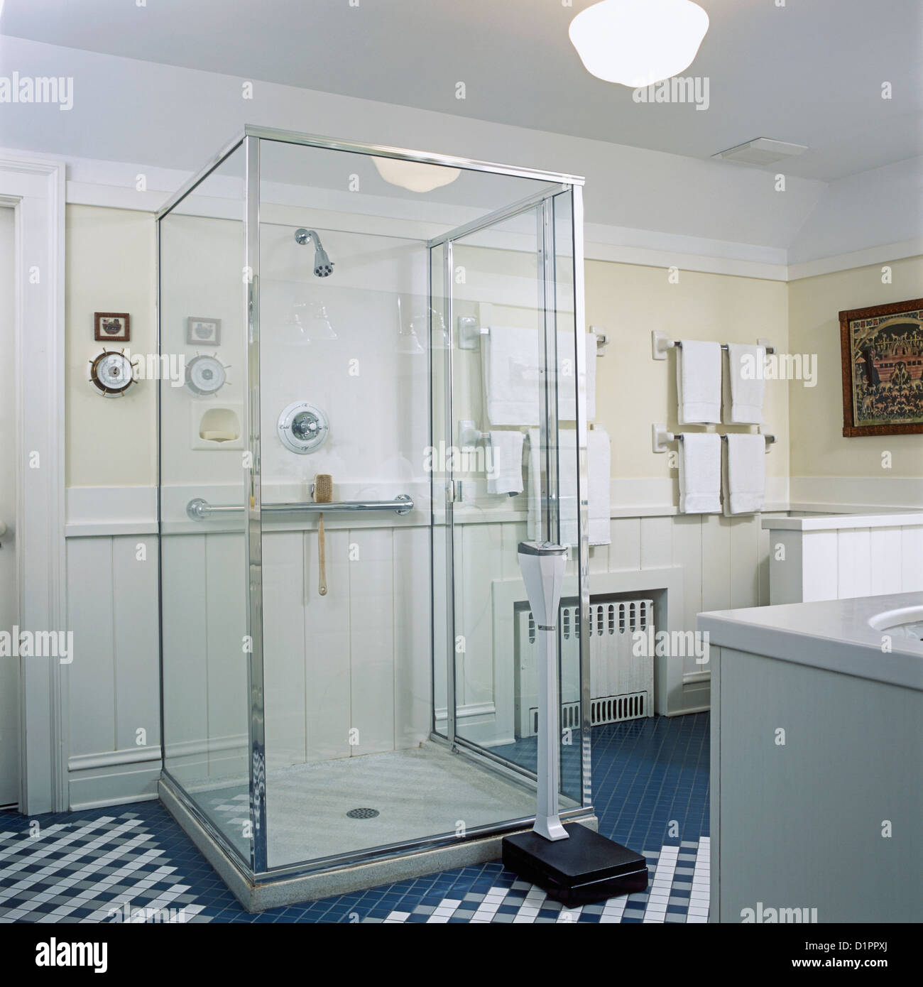 BATHROOMS: View towards glass box shower stall, teal blue and white tile floor, weighing scale, white towels. Stock Photo